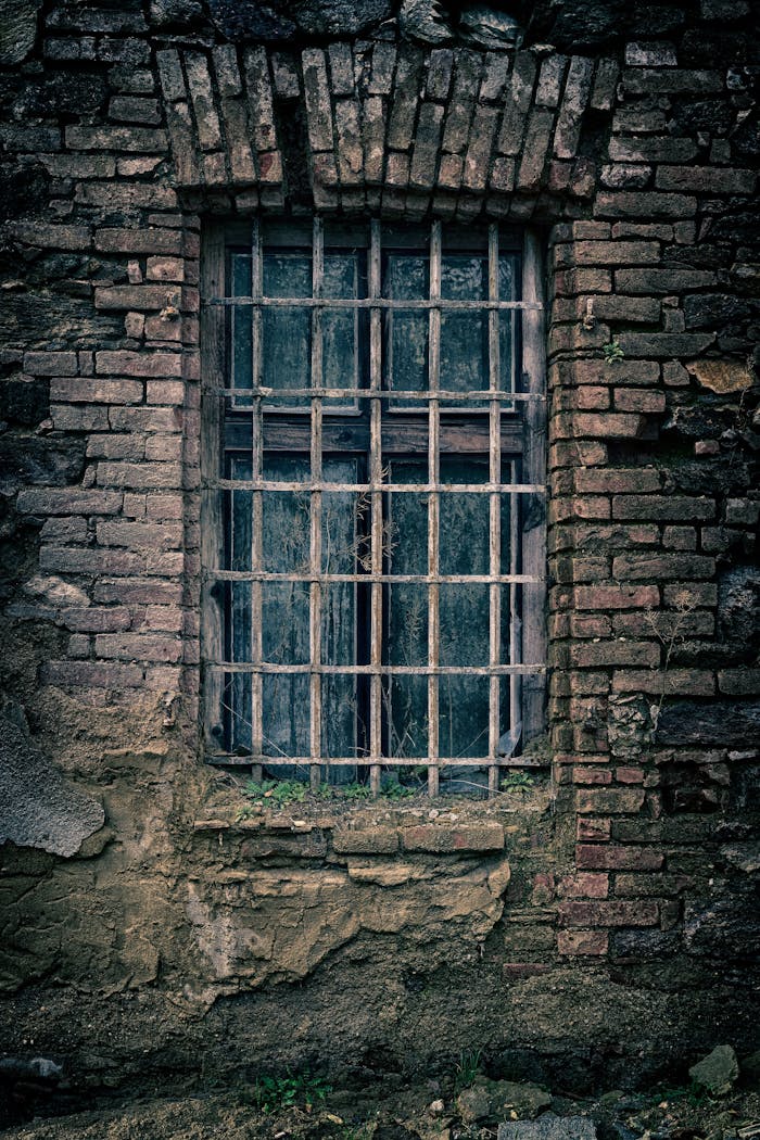 A moody close-up of an old brick wall featuring a barred window, capturing a sense of nostalgia.